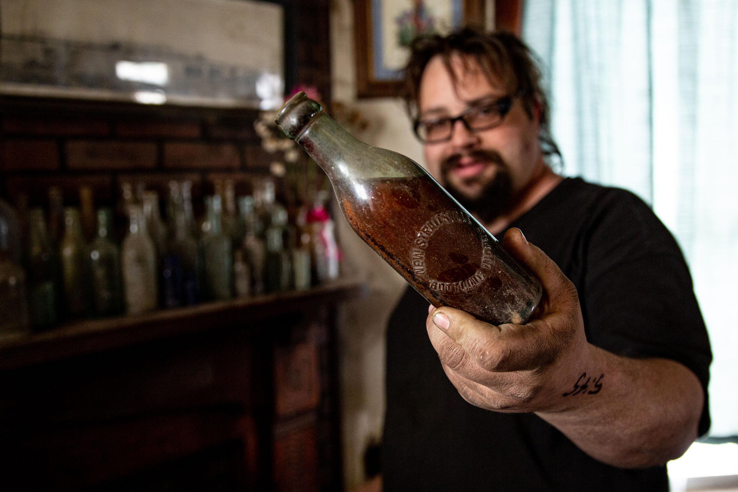  Cam Blosser holds up a bottle full of soda from the early 1900s preserved due to a broken of cork. Cam found the bottle in the creek behind his home in New Straightsville. Talking to “old timers” in the area, Cam learned that before refrigerators, bottles of soda like this were put in the creek to cool off. He surmises this one was forgotten in the creek and was washed down stream and buried until he discovered it.  